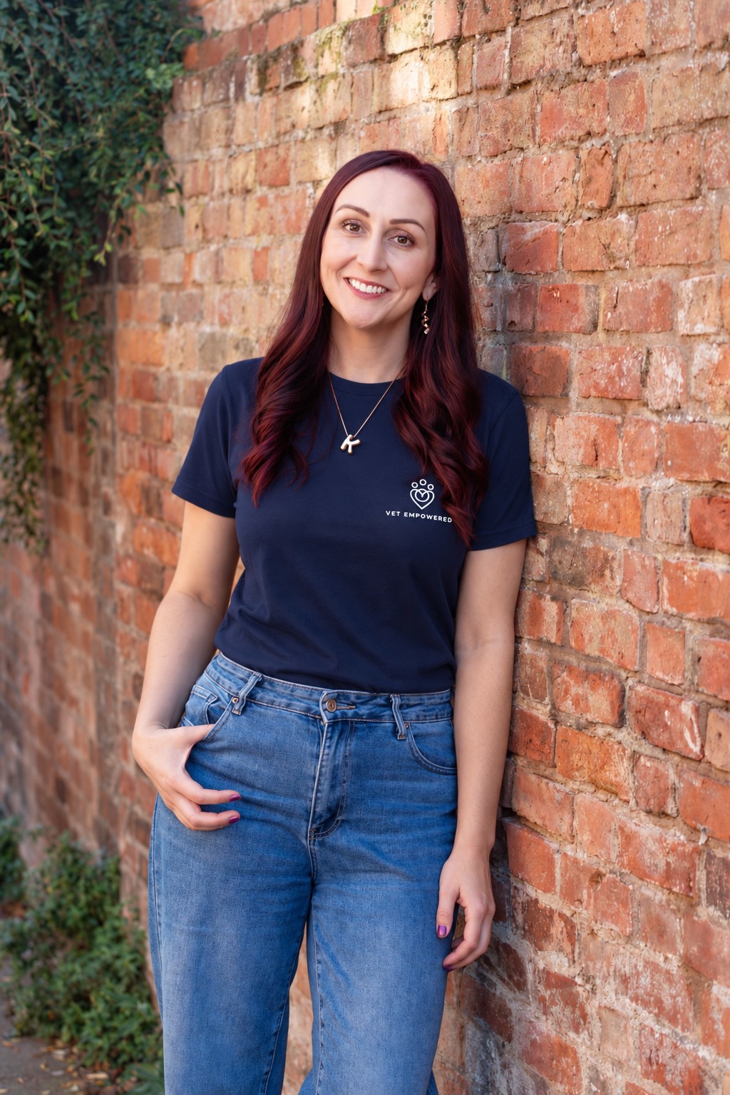 Dr Katie Ford in a navy Vet Empowered T-shirt, smiling against a brick wall