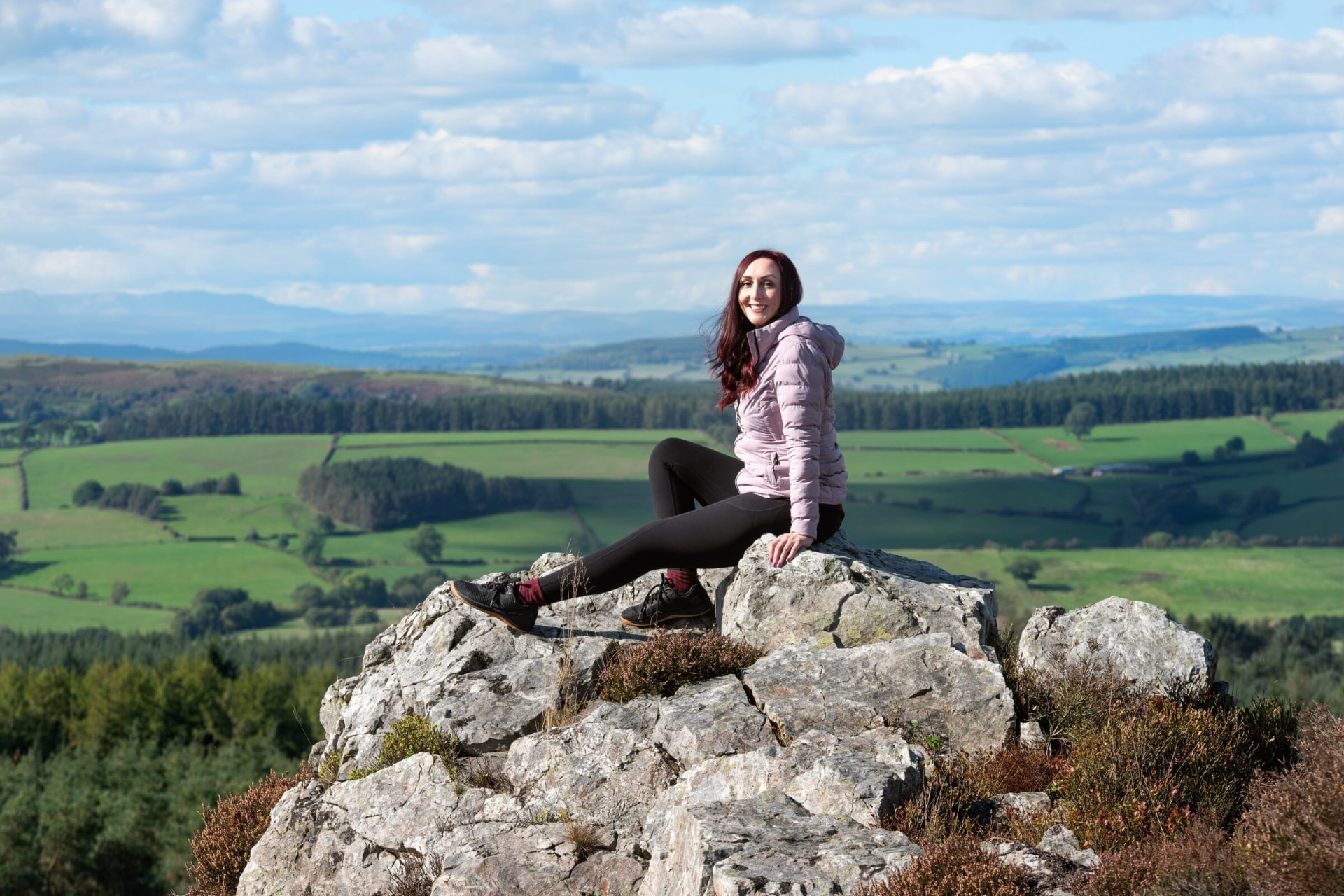 Katie sitting on a rock high above a wide green valley