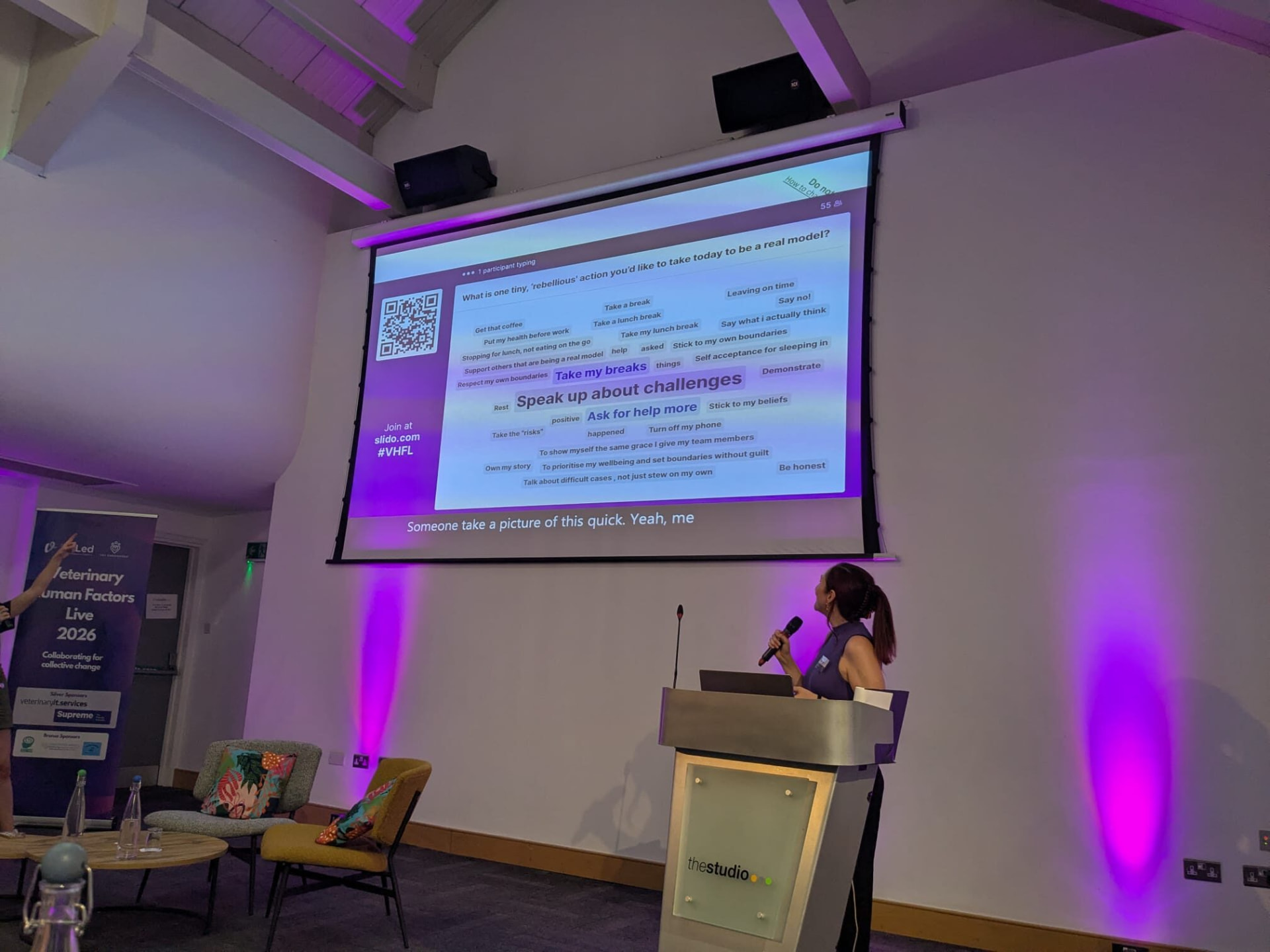 Dr Katie Ford speaking at a lectern beside a large screen