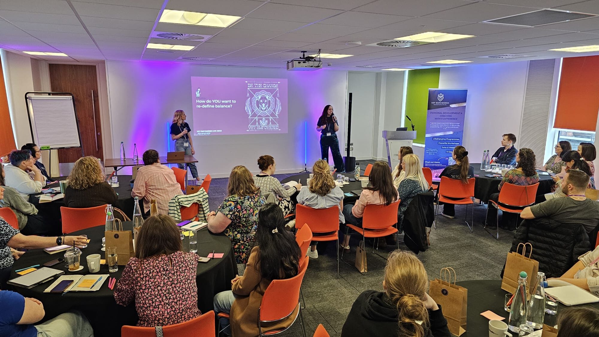 Katie Ford and Claire Grigson on stage in front of a full room at Vet Empowered Live