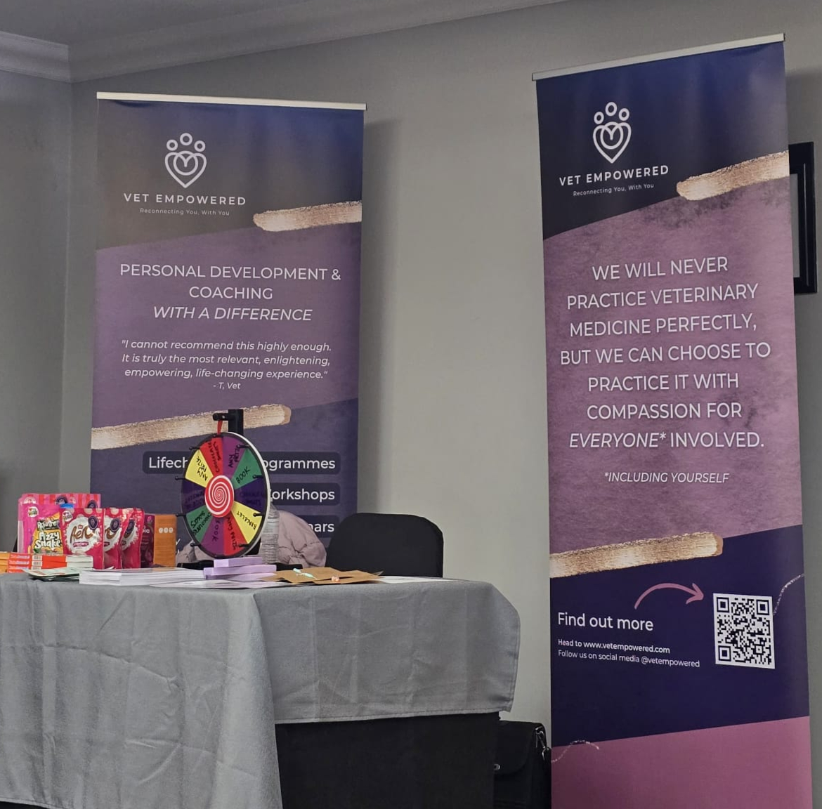 Table with colorful wheel and snacks against two Vet Empowered banners on personal development and veterinary compassion.
